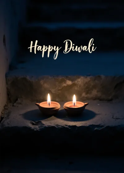 Two clay lamps lit on a stone step at dusk. Happy Diwali.